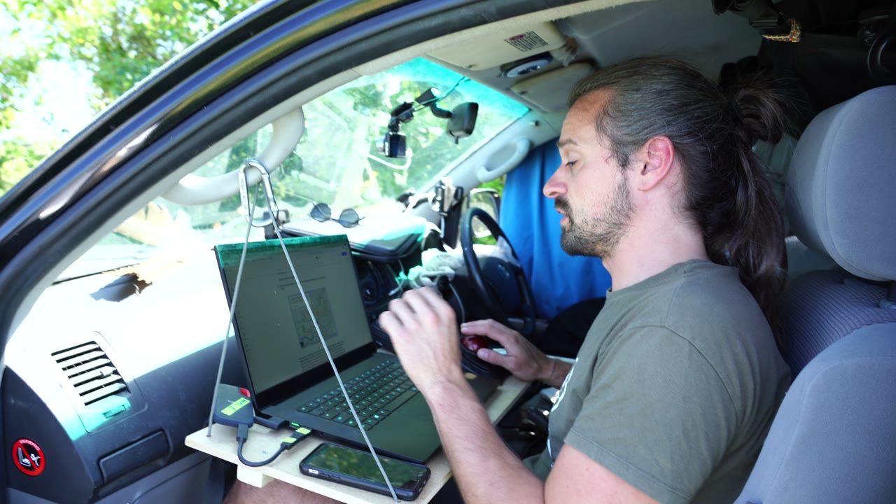 Axel typing on a laptop on a home-made desk in the front seat of his van