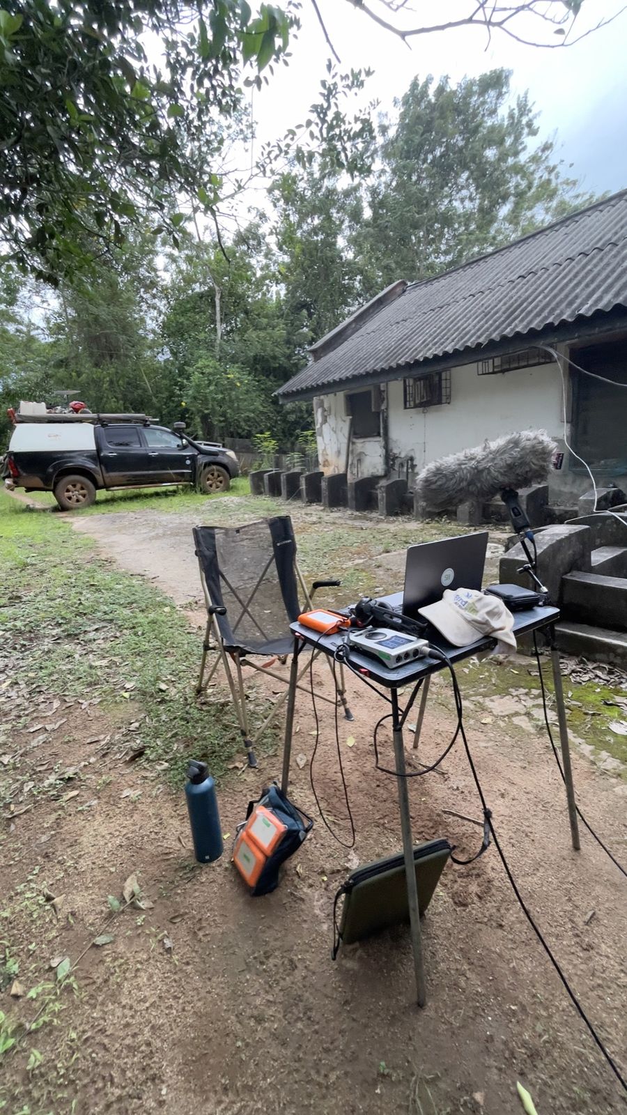 A folding table with a laptop and recorder outside a forest station, the truck parked behind