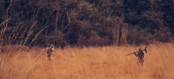 Axel and Moises walking through tall dry grass in Liberia with recording gear
